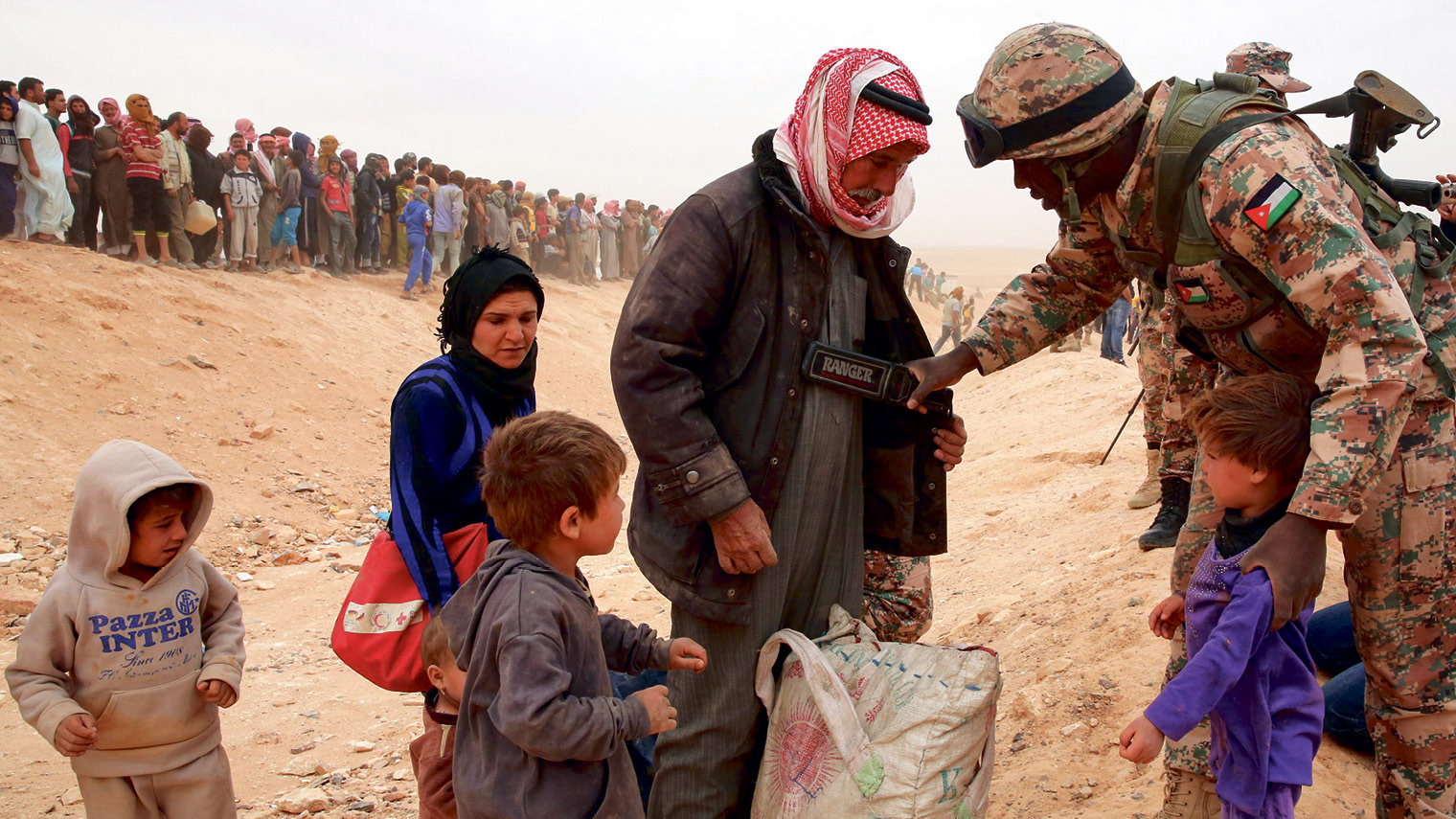 A Jordanian soldier scans newly arrived Syrian refugees as they wait to cross the border - KHALIL MAZRAAWI/AFP/Getty Images