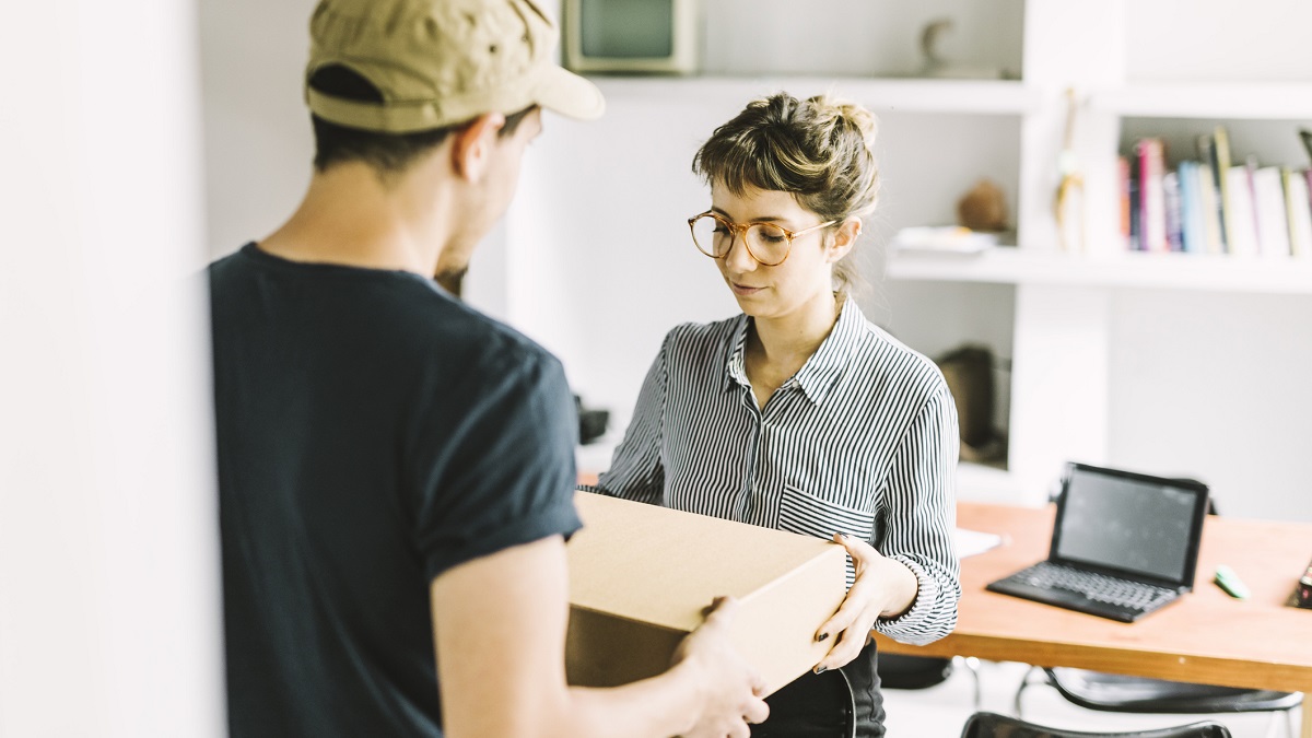 Young woman receiving a parcel from delivery man at co-working space.