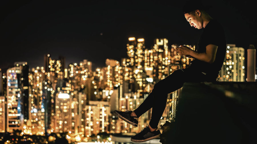 A young man looking at a smart phone overlooking the city