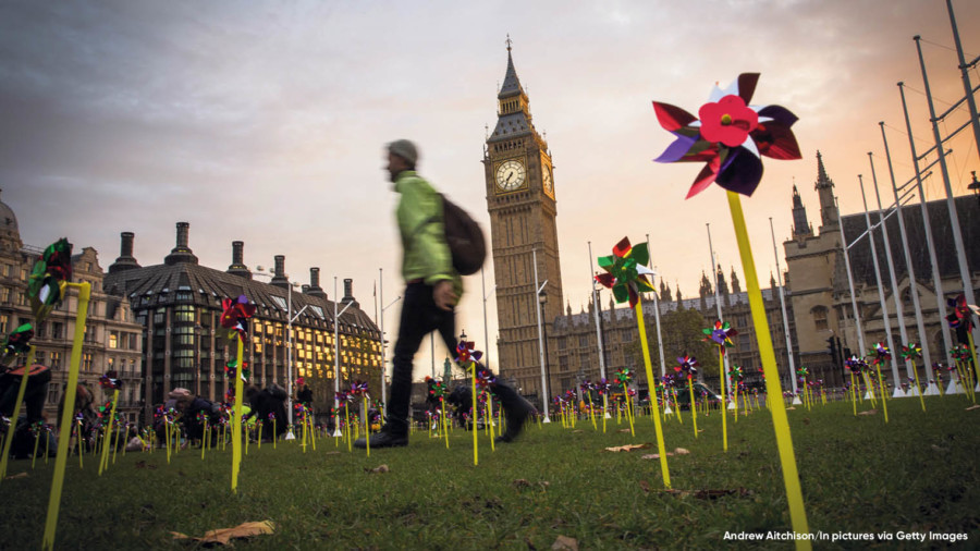 Person walking past Westminster with pinwheels on the grass