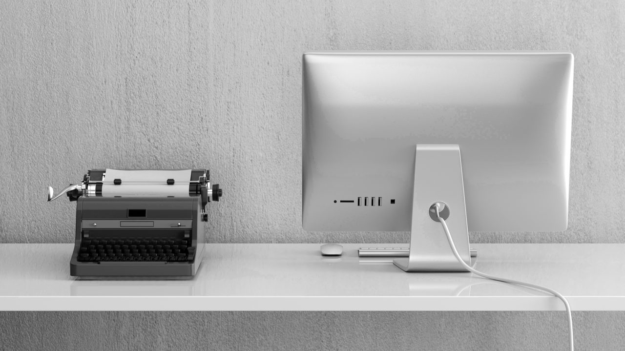 Black and white picture of typewriter next to Mac desktop illustrating digital transformation