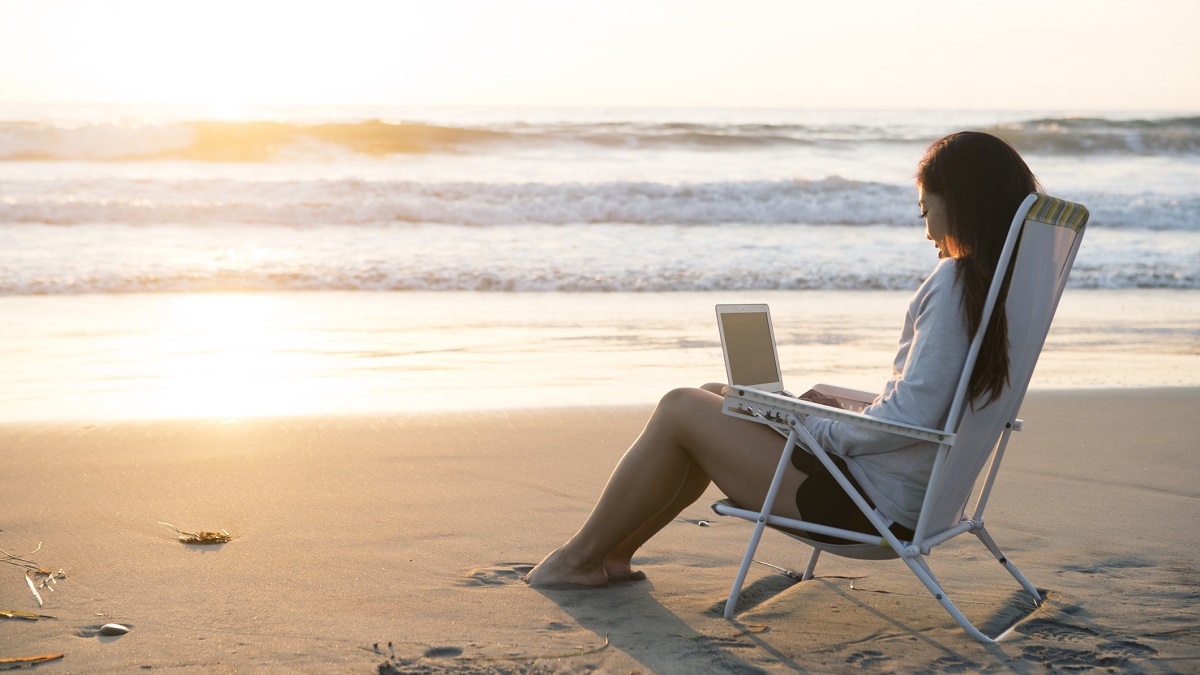 Young woman sitting by the beach working on a laptop