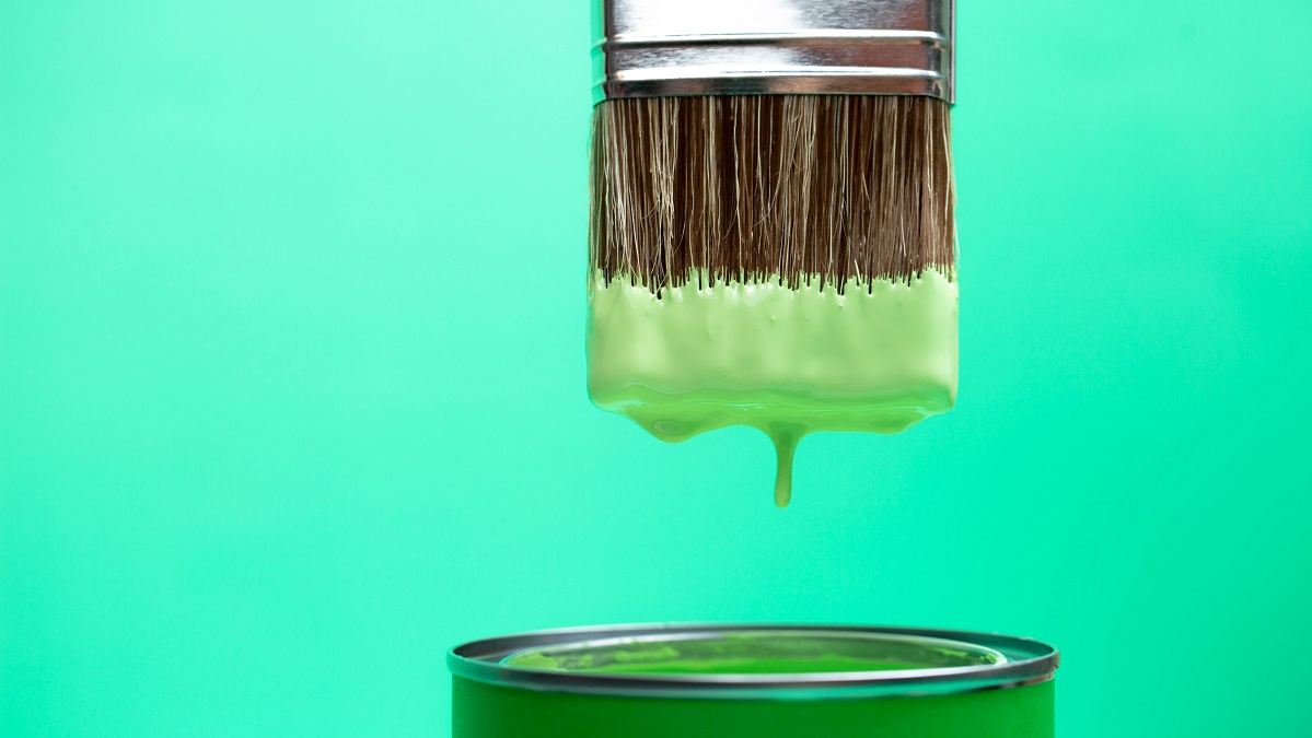 Green paint dripping from brush into jar
