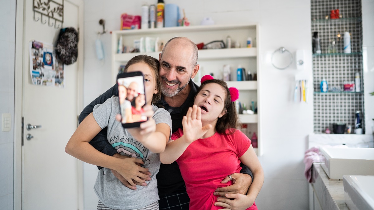Father with daughters doing a video or taking a selfie on smartphone at home - including a special needs girl