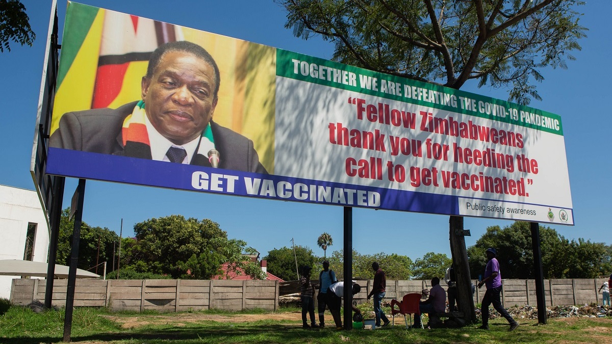 HARARE, ZIMBABWE - NOVEMBER 30: People seek shade under a billboard of Zimbabwe's President encouraaging citizens to get vaccinated on November 30, 2021 in Harare, Zimbabwe. Zimbabwe is among the southern African countries facing travel bans after the Omicron Covid-19 variant was first reported in neighboring South Africa. Its vice president and health minister urged people not to panic, and said the country's vaccination program - which has the goal of inoculating 60% of Zimbabweans by year's end - would prepare it for another wave of infections. Zimbabwe has fully inoculated around 2.8 million people since February, about 20% of its population. (Photo by Tafadzwa Ufumeli/Getty Images)