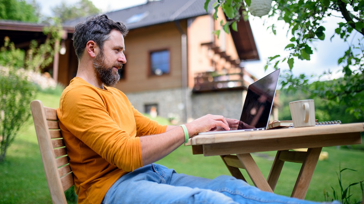 Side view of mature man with laptop working outdoors in garden, home office concept.