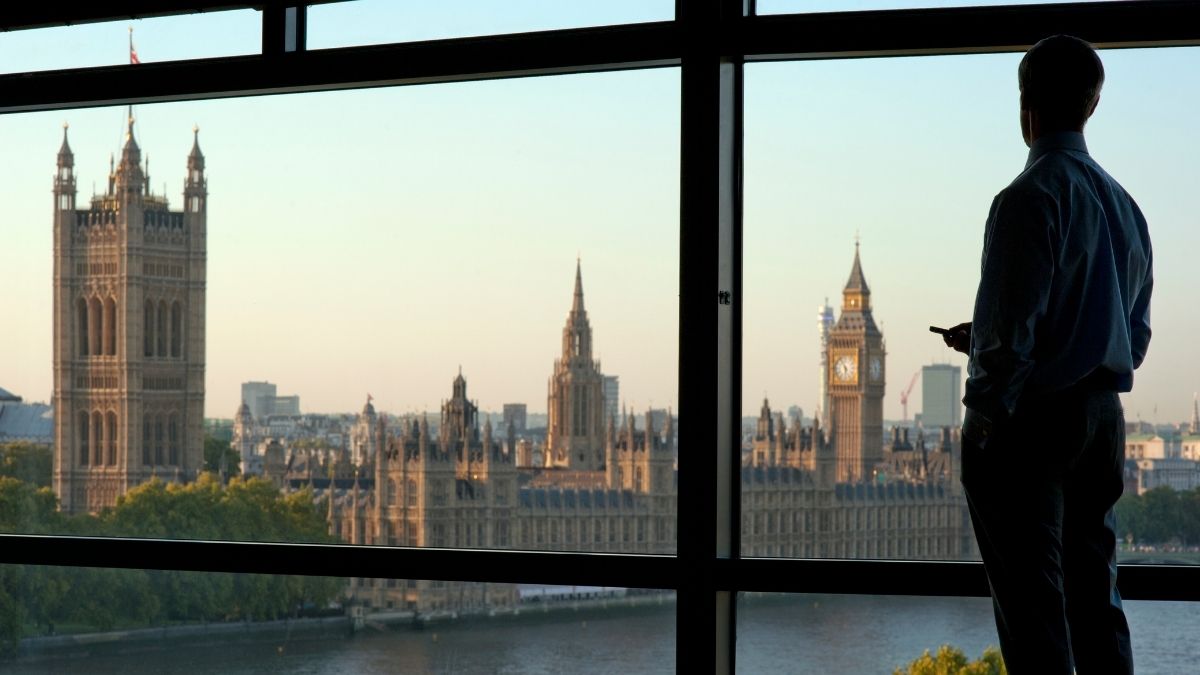 Man looking out office window towards the houses of parliament