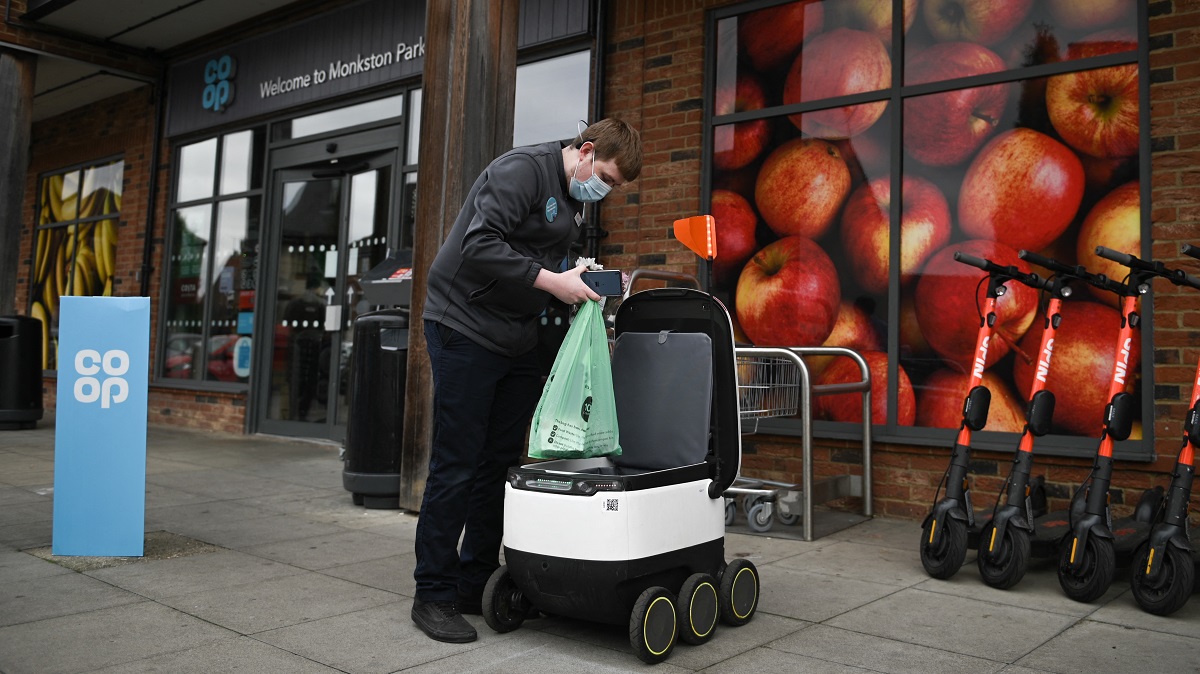 A man loads a shopping bag into a delivery robot outside a Co-op supermarket in Milton Keynes