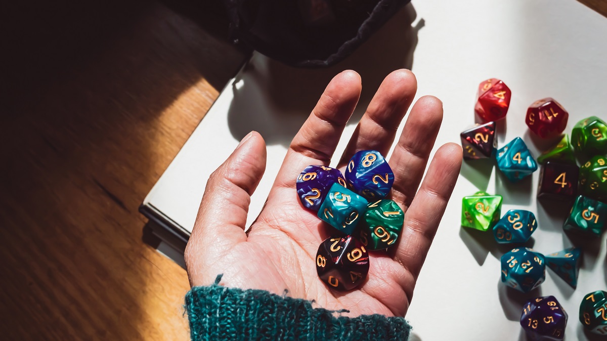 Image of a hand holding various colored and shaped role-playing dice lit by sunlight