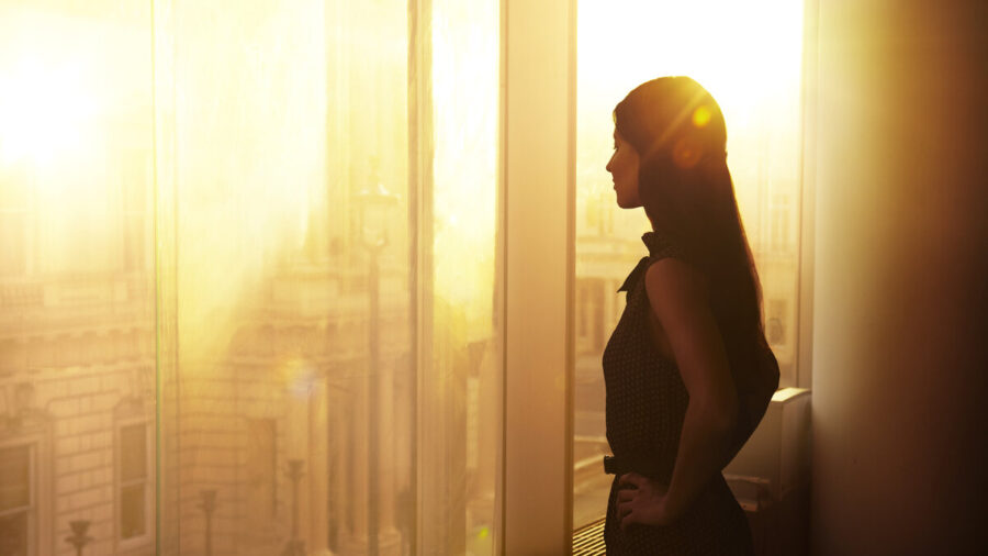 Business woman looking out of a window toward a setting sun