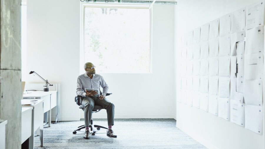 Businessman sitting in a well-lit office considering business plans posted on the office wall
