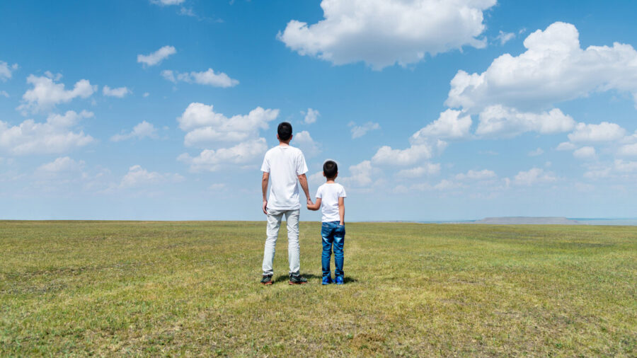 Father and son looking at clouds in an open field