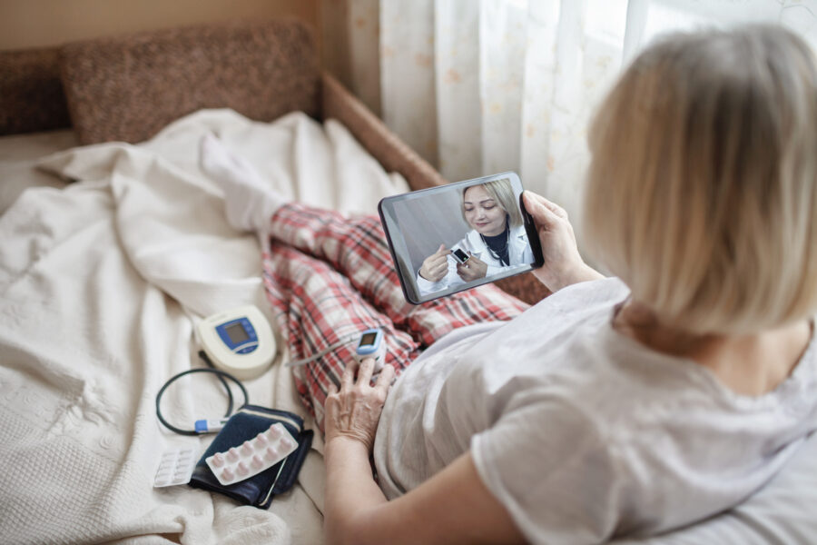 Old Woman In Bed Looking At Screen Of Laptop And Consulting With A Doctor Online At Home, Telehealth