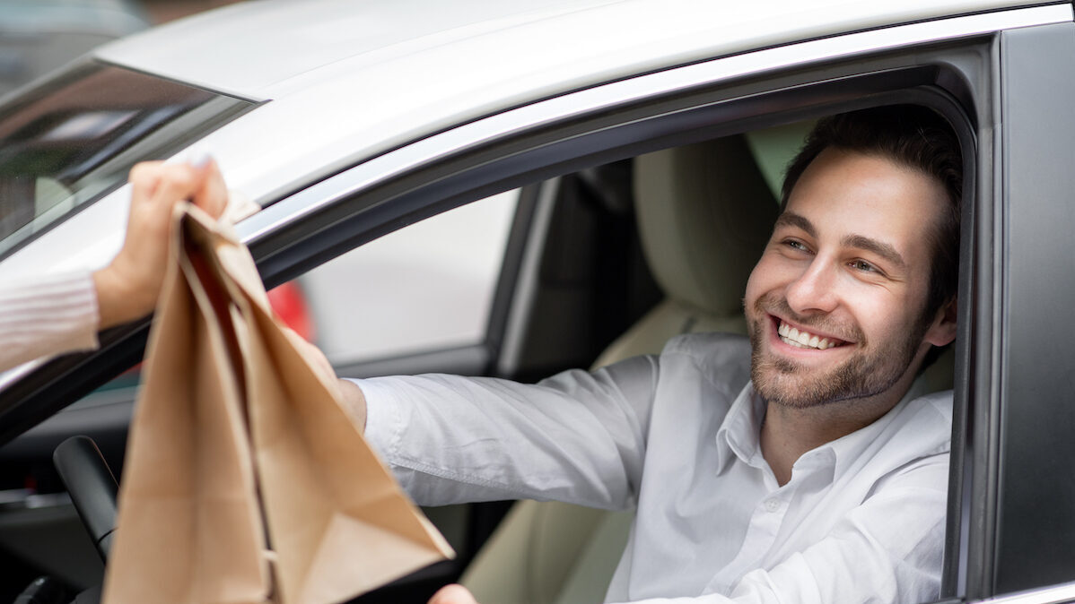 Food,delivery,courier,gives,paper,bags,to,man,in,car.