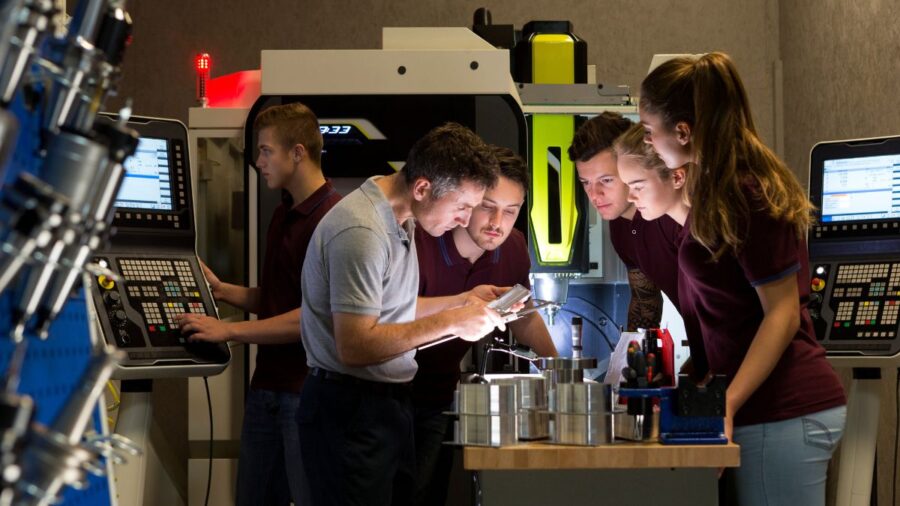 Apprentices gather around a piece of technical manufacturing equipment as their taught by an employee how to use it